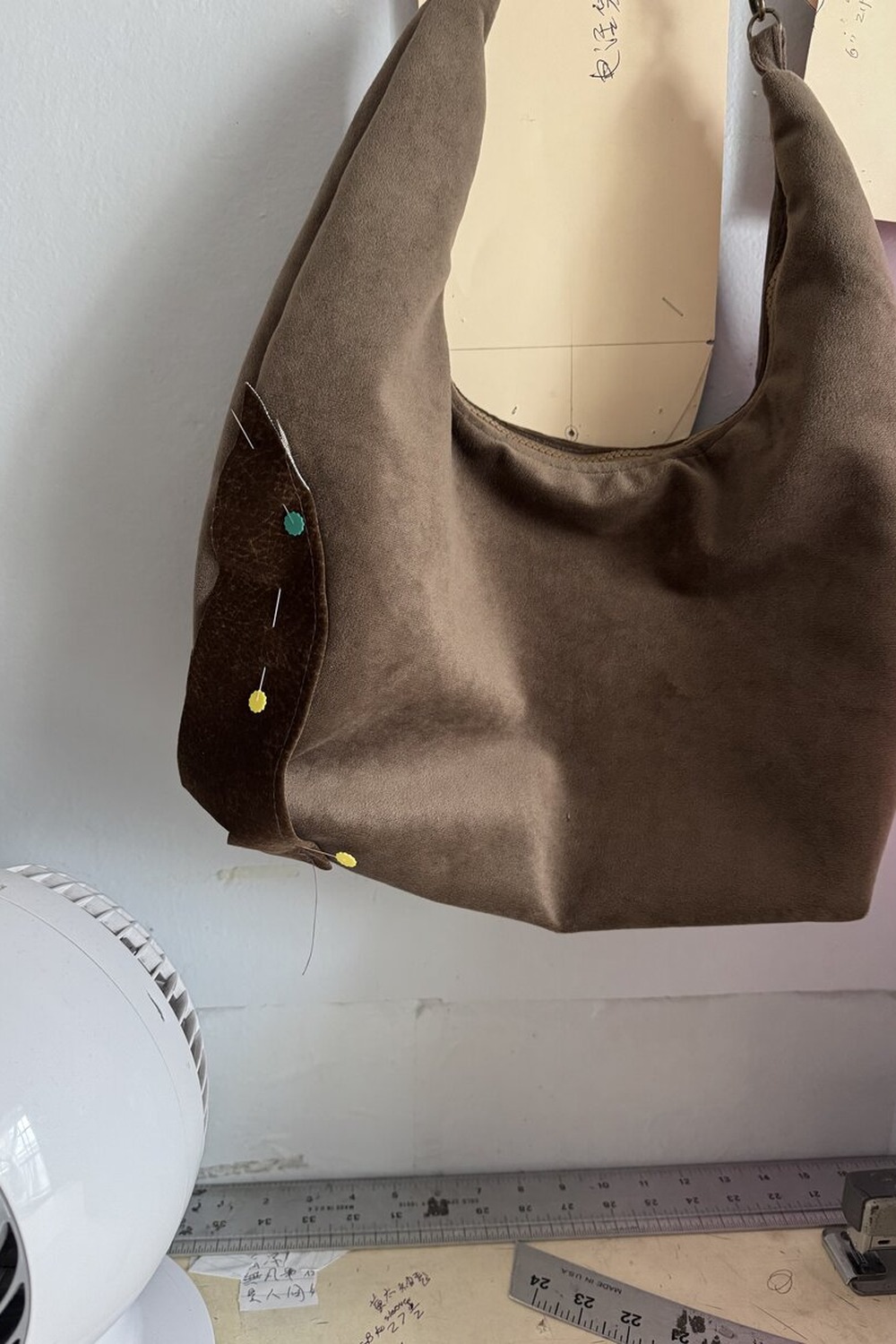 Half-finished velvet hobo with a leather corner being pinned, with Chinese pattern notes behind.